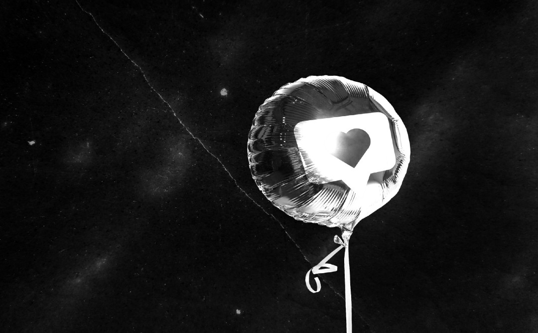 Runder Luftballon auf schwarzem Hintergrund, auf welchen ein Herz ist